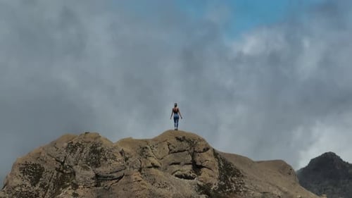 Brave woman raising arms in freedom on high rocky mountain peak, adventure concept