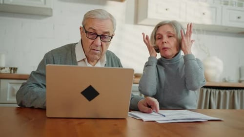 Senior Couple Discuss Finances at Table with Laptop