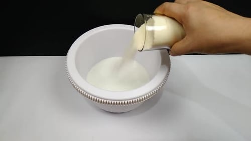 Eine Frau fügt der Milch in die Pfanne Eiscremepulver hinzu, um sie zu vermischen und Eiscreme zuzubereiten