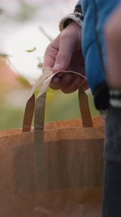 Primer plano de una persona con chaqueta azul caminando cortando hojas y colocándolas en una bolsa de papel