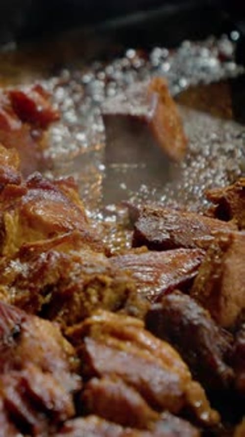 Vertical video Pieces of pork meat and sausages cooking in a hot pan