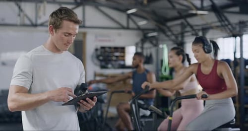 Gym trainer using digital tablet to monitor his HIIT group fitness class