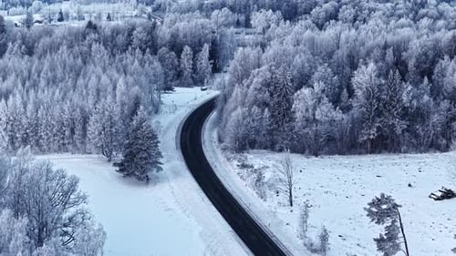 Winter Drone Following a Winding Road Through Snow Covered Forest