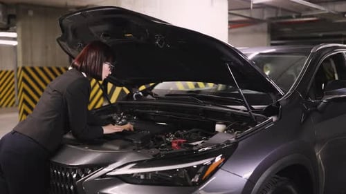 Woman Examining Car Engine in Parking Garage