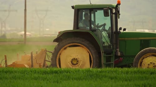 tractor verde arando un campo de cereales entre montañas