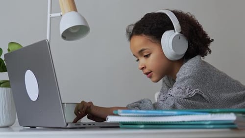 Primary School African American Student Child with Headphones Hand Writing in Book Using Laptop