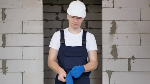A Male Construction Worker in a Protective Helmet and Glasses Wears Blue Gloves