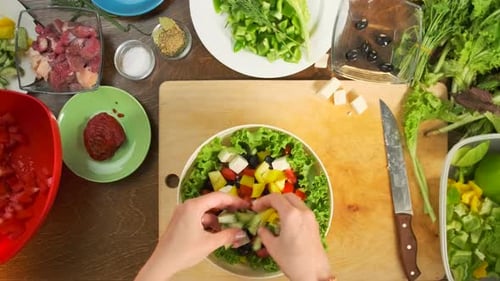 Cooking chef hands are sprinkling vegetables on a vegetable plate on the kitchen table.