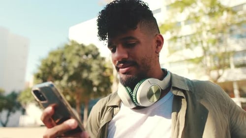 Close up, young man with headphones sits on bench and uses cellphone
