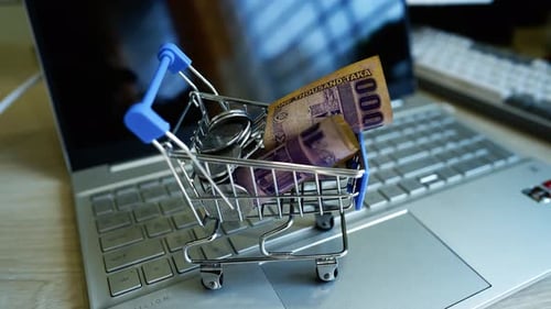 Coins and Currency in Miniature Shopping Cart on Laptop