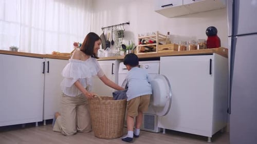 Schöne asiatische Mutter bringt ihrem jungen Sohn bei, schmutzige Kleidung im Haus zu waschen.