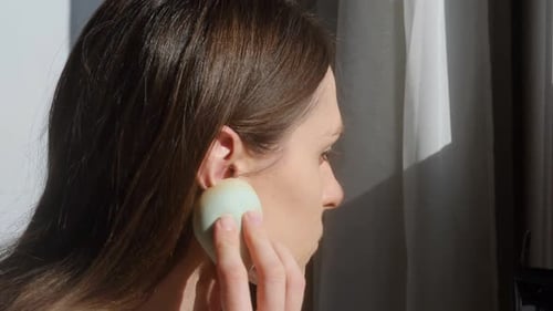 Woman Applying Makeup with Sponge in Natural Light