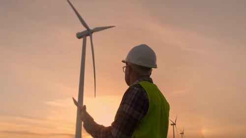 Young Maintenance Engineer Man Working in Wind Turbine Farm at Sunset