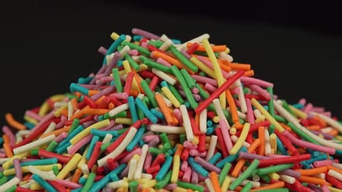 Colored confectionery sprinkles rotating close up on black background. Culinary topping