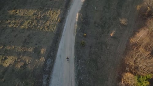 A lone cyclist rides along a dirt path through a rural landscape captured from above