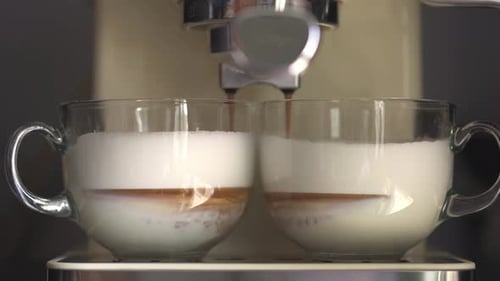 Close Up Of Black Coffee Flowing Into A Transparent Cup With Whipped Milk. Making Cappuccino