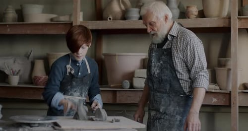 Caring Grandfather Teaching Boy to Work with Clay in Traditional Pottery Workshop
