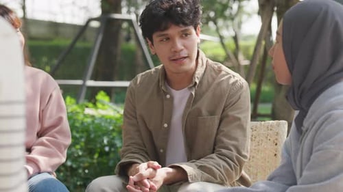 Small Asian group of people sit in a close circle and talk to a therapist in park.