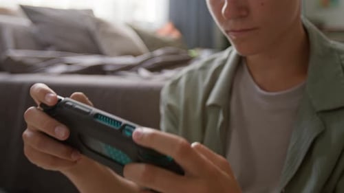 Teenage Boy Plays Handheld Video Game Device at Home