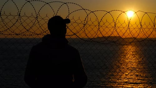 Man Silhouette Behind Barbed Wire Fence at Sunset