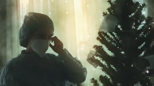 Closeup of the Sad Doctor in Protective Suit and Visor Decorates the Christmas Tree with Medical