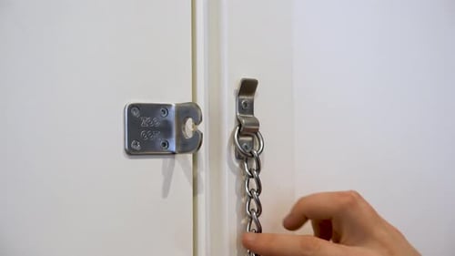 Male hands locking a door chain lock.