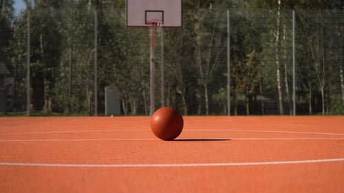 Basketball Lies in Center of Fenced Basketball Court in Empty Street Court
