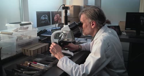 Microbiólogo maduro analisa amostra sob microscópio no laboratório de ciências arqueológicas