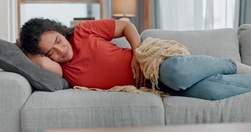Stomach ache, stress and woman on a sofa with pms, endometriosis or bad gut health at home