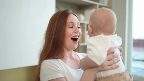Mother holds her baby indoors smiling lovingly