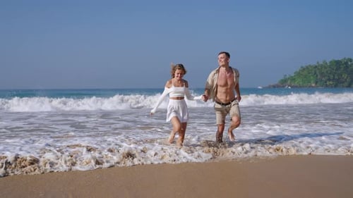 Attractive Couple Run Holding Hands in Sea Surf Waves Tanned Man and Woman Having Fun on Summer