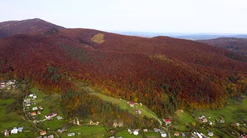 Aerial View of a Rural Village with Small Houses Between Autumn Mountain Hills Covered with Yellow