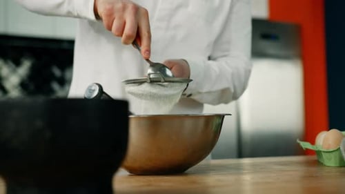 sifts flour with a spoon to the cooking bowl in a professional kitchen. Making dough in a restaurant