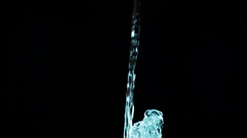 A stream of water falls and creates a splash on a black background. Slow motion.