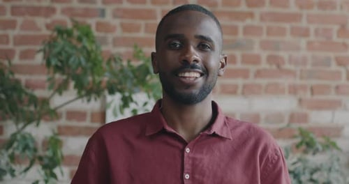 Portrait of Young African American Man Looking at Camera with Serious Face Then Smiling Against