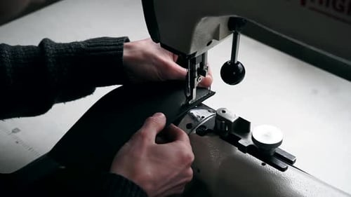 Close-up of the tailor's hands. Close-up sewing machine. The tailor sews a purse made of leather