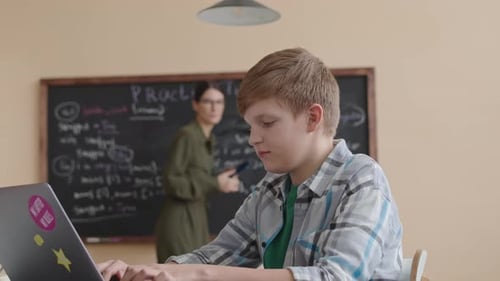 Boy Typing on Laptop with Teacher Helping