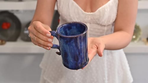 Woman in white dress showing a blue cup, final result at pottery workshop