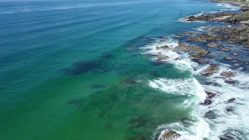 Aerial shot looking at the clear turquoise sea crashing against the rocks on the west coast of Scotl