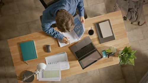 Overhead View Professional Analyzing Business Charts and Working on Laptop