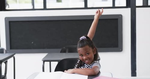 In a school classroom, a young African American girl raises her hand