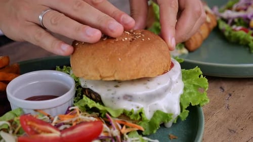 Hands Placing Bun on Delicious Burger with Salad