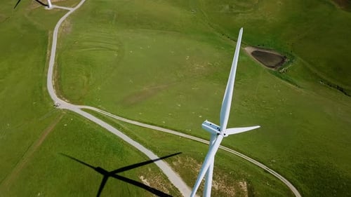 Aerial view over a wind power turbine and summer green field - reverse, drone shot