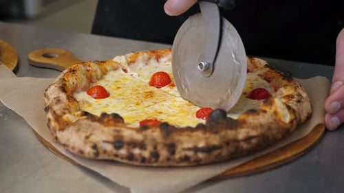 The Cook Uses a Round Knife to Cut the Pizza Into Pieces in a Pizzeria