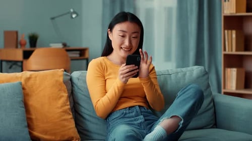 Smiling Woman Uses Smartphone on Living Room Couch