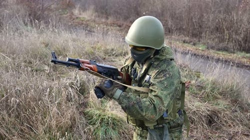 Camouflaged Soldier Loading Assault Rifle in Rural Field