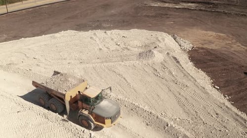 Bird's eye view of a dump truck full of dirt and rocks on a dirt trail.