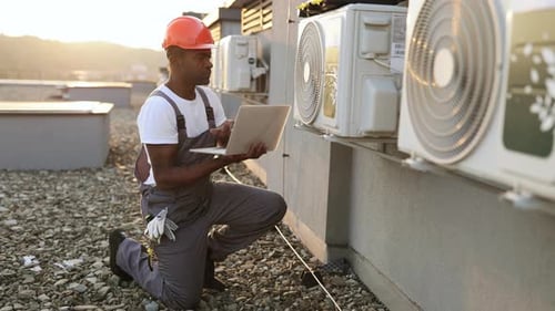 HVAC Technician Inspecting Units on Rooftop at Sunset