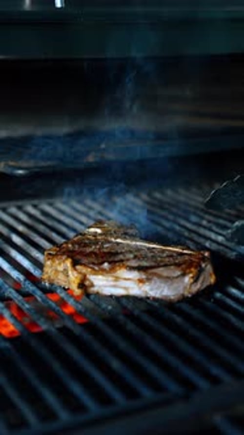 Unrecognized cook turns a piece of meat on the grill with the help of tongs. Close up.
