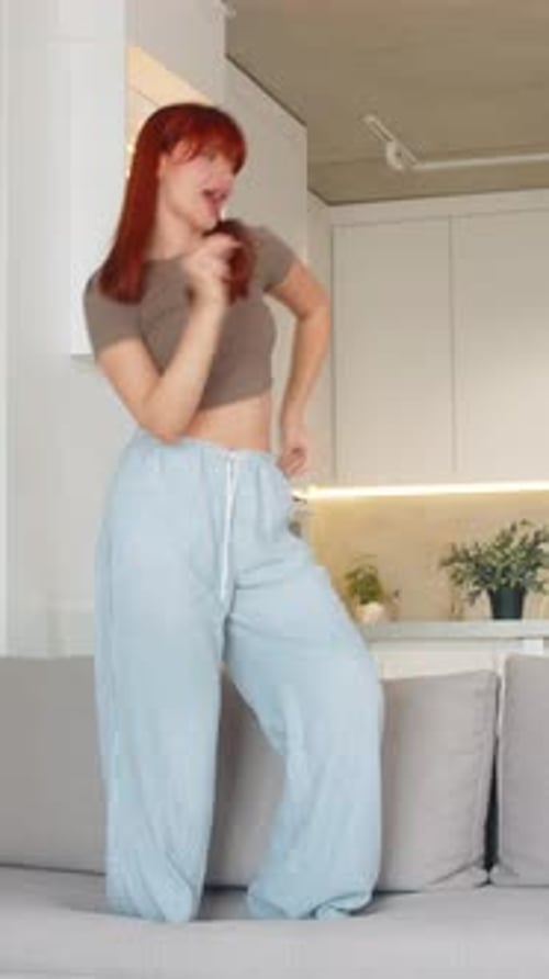 Excited Woman Dancing on Sofa in Modern Apartment